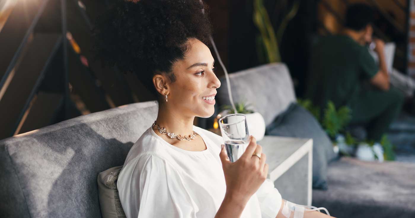Happy woman, water and wellness in clinic with iv drip, detox and antioxidants for hydration benefits. Person, smile and liquid in medical spa with intravenous fluid, vitamins or minerals for health.