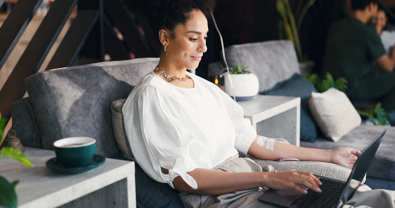 Woman, relax and laptop in clinic, iv drip and happy for recovery with fluid, writer and remote work. Healthcare, nutrition and person with tech for freelance article, typing and immune system boost